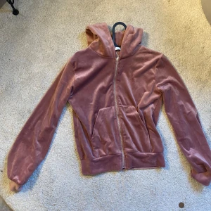 Rosa velour hoodie med dragkedja - Mysig hoodie i rosa velour med huva och dragkedja framtill. Jackan har långa ärmar, ribbade muddar och två fickor framtill. Perfekt för en avslappnad och trendig look.