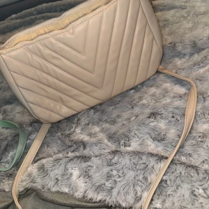 Beige quiltad axelväska med kedjedetalj - Säljer en beige axelväska med quiltat mönster och guldfärgad kedjedetalj på axelremmen. Väskan har dragkedja upptill och ett innerfack med dragkedja. Perfekt storlek för det viktigaste och stilren design.