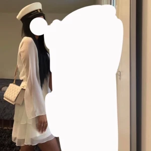 Vit klänning med volang - Säljer en vit omlottklänning med långa ärmar och volangdetaljer. Klänningen har v-ringning och smock i midjan för en bekväm passform. Perfekt för student eller sommarens tillfällen. 