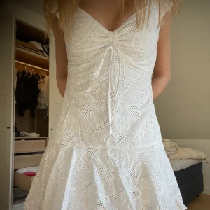 Vit kortklänning med broderade blommor och knyt - Superfin vit kortklänning med broderade blommor och knyt framtill. Klänningen har v-ringning, korta ärmar och volang i nederkant inte mina bilder så skriv för egna 💗.  