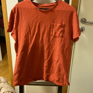 Röd t-shirt med bröstficka - Säljer en enkel röd t-shirt från Cubus i storlek L. T-shirten har en klassisk passform, rund halsringning och en liten bröstficka på vänster sida. Perfekt till vardags och lätt att matcha med jeans eller shorts. Rostbrun typ 