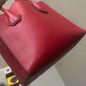 Röd handväska från Michael Kors - Säljer en snygg röd handväska från Michael Kors i skinn med guldfärgad MK-detalj. Väskan har två handtag och en stilren, klassisk form. Perfekt för dig som vill ha en färgklick till din outfit!