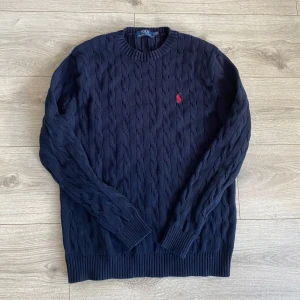 kabelstickad  Polo Ralph Lauren - Säljer en mörkblå kabelstickad tröja från Polo Ralph Lauren med rund halsringning och röd broderad logga på bröstet. Riktigt fet tröja som jag tyvärr inte använder längre, Skriv vid funderingar