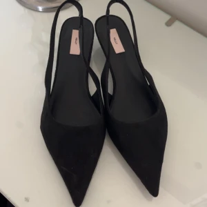 Svarta pumps med låg klack från Nelly - Säljer ett par svarta pumps från Nelly med spetsig tå och låg klack. Skorna har öppen häl och smala remmar som ger en stilren look. Perfekta för dig som vill ha en klassisk och elegant sko. Klacken är 3 cm, Dom är endast använda EN gång! 🩷