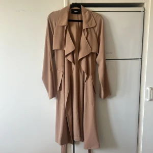 Beige trenchcoat från Bik Bok - Säljer en beige trenchcoat från Bik Bok i storlek XS. Jackan har långa ärmar, öppen front med breda slag och ett bälte i midjan. Finns i Kristinehamn och kan skickas mot fraktkostnad eller mötas upp🤍