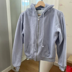 Ljuslila hoodie med dragkedja från Brandy Melville - Mysig ljuslila hoodie från Brandy Melville med dragkedja framtill och justerbar huva. Tröjan har två fickor och ribbade muddar vid ärmslut och nederkant. Perfekt för en avslappnad stil. Skick enligt bild. 