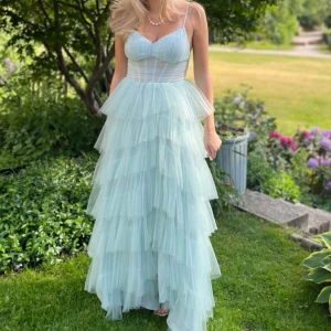 Turkos balklänning med volanger - Elegant turkos balklänning med flera lager av volanger och smala axelband. Klänningen har en slits vid ena benet och har en släp designad därav är den längre där bak. Endast använd en gång på balen i 9an förra sommaren. Skriv om du har några frågor! 💞💞