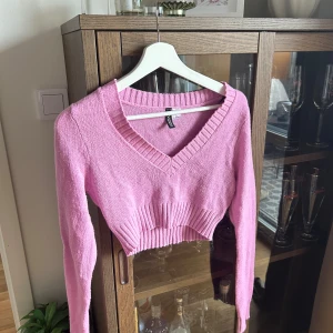 Rosa croppad stickad tröja från H&M - Säljer en ljusrosa croppad stickad tröja från H&M. Tröjan har v-ringning, långa ärmar och ribbade detaljer vid midjan och ärmsluten. Perfekt för att ge en söt touch till din outfit!