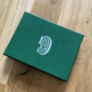 Grön korthållare  - Säljer en exklusiv grön korthållare från  med deras ikoniska mönster i vitt och gult. Korthållaren har flera fack för kort och är tillverkad i skinn med tryckt logotyp framtill. Perfekt accessoar för dig som vill ha något unikt och stilrent.