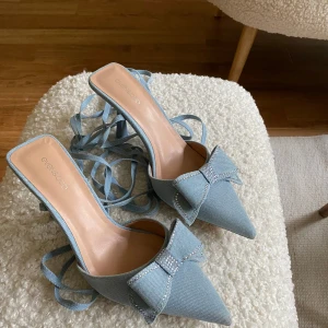 Ljusblå pumps med rosett och snörning - Säljer ett par ljusblå pumps med spetsig tå, hög klack och dekorativ rosett framtill. Skorna har långa snören som kan lindas runt vristen. Nyköpta för en vecka sedan, aldrig använda, storlek 37 (passar mellan storlekarna 36-38). Råkade slänga tillhörande skokartong samt etiketter och kan därför inte returnera. Säljer därav dessa superfina skor.