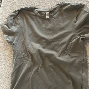 Grå basic t-shirt från H&M - En enkel grå t-shirt från H&M Basic-kollektionen. T-shirten har rund halsringning och korta ärmar, tillverkad i mjuk bomull. Perfekt för en avslappnad och stilren look.