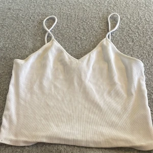 Vit ribbad linnetopp från Monki - Säljer en vit ribbad linnetopp från Monki med smala axelband och v-ringad hals. Perfekt för varma dagar eller som layering-plagg. Enkel och stilren design som passar till mycket.💕
