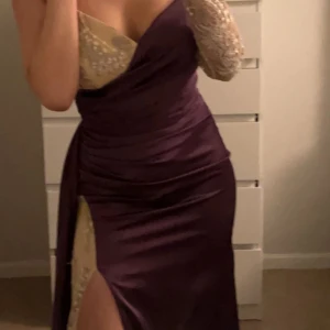 Lila långbalklänning med spetsdetaljer - Säljer en elegant lila långbalklänning med beige spets upptill och en hög slits framtill. Klänningen har en omlottkänsla och figurnära passform, perfekt för speciella tillfällen. Snygg axelbandslös design med v-ringad urringning. Den har även blivit skräddarsydd till min längd och jag är 163, ärmen som man ser på bilden togs även bort.