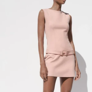 Ljusrosa ärmlös miniklänning med bälte - Säljer en ljusrosa ärmlös miniklänning med rund hals och matchande bälte i midjan. Klänningen har en figurnära passform och är perfekt för sommarens tillfällen. Enkel och stilren design som ger en elegant look.