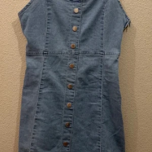 Jeansklänning med knappar st 36 - Säljer en ljusblå jeansklänning från Amisu med knappar framtill. Klänningen är ärmlös och har en rak passform. Perfekt för en avslappnad stil och enkel att matcha med olika accessoarer. New Yorker är den köpt på och är i absolut nyskick. St 36. Banden är ställbara och då perfekt till detta års mode i denim!  Fina axelband och den är stretchig. Knapparna är fast så ingen risk att dom går upp när dom används. 