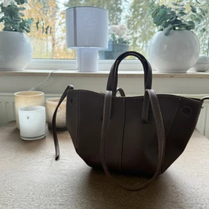 Mörkbrun väska  - En mellanmodel av väska.2 olika handtag. Kommer inte ihåg var den är ifrån men den är aldrig använd. 