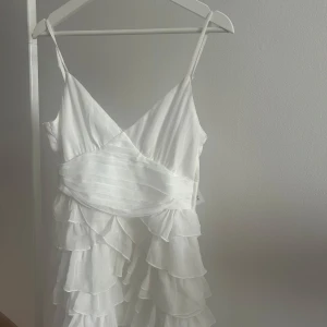 Vit volangklänning med smala axelband - Vit volang klänning med smala axelband. Perfekt till studenten eller andra tillställningar. Har aldrig använt klänningen och prislappen sitter kvar. Anledningen till att jag säljer den är för att jag har hittat en annan studentklänning. Köparen står för frakten🌺☀️🏝️