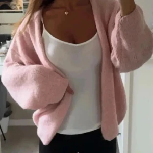 Ljusrosa stickad kofta - Mysig ljusrosa stickad kofta med lös passform och långa ärmar. Perfekt att slänga över en topp för en avslappnad look. Koftan är öppen framtill och har en fluffig känsla.