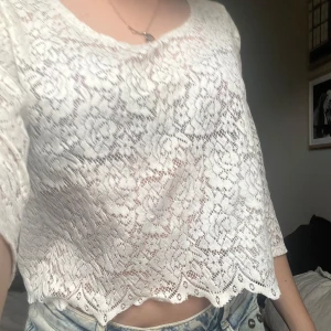 Vit spetsblus från Monki - Säljer en vit blus från Monki i spets med blommigt mönster. Blusen har trekvartsärm och är croppad med vågig nederkant. Perfekt att styla över ett linne eller bikini.