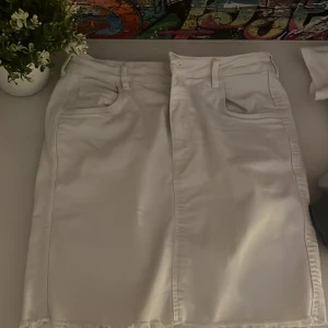 Vit jeanskjol från denim - Säljer en klassisk vit jeanskjol från Adenim med fickor fram och bak samt hällor för bälte. Kjolen har en rak passform och är perfekt för en fräsch och stilren look. Passar till många olika outfits!