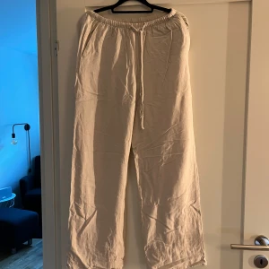 Beiga linnebyxor från Gina Tricot - Säljer ett par beiga linnebyxor från Gina Tricot med resår i midjan och dragsko. Byxorna har raka, vida ben och är tillverkade i ett lätt och luftigt material som passar perfekt för varmare dagar.