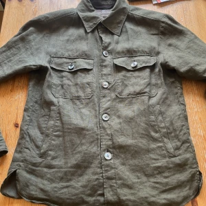 Olivgrön overshirt från Oscar Jacobson - Säljer en olivgrön overshirt från Oscar Jacobson i linne. Jackan har klassisk krage, fyra knappar framtill, två bröstfickor med lock och knappar samt två snedställda sidfickor. Perfekt för lager-på-lager och stilren look. Använd ett fåtal gånger och är i storlek S! Nypris 3000kr, Hör av dig vid frågor🤗