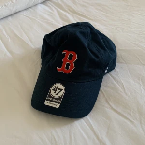 Svart keps från 47 Brand med röd B - Svart keps från 47 Brand med en stor röd B broderad framtill. Justerbar passform med klassisk böjd skärm. Perfekt för dig som gillar sportig stil eller vill ha en snygg accessoar till vardags.