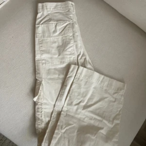 Cargopants från Monki - Snygga krämvita cargopants med raka ben och flera stora fickor på sidorna. Byxorna har normal passform och är tillverkade i bomull, vilket gör dem både bekväma och stilrena. Perfekta för en avslappnad look.