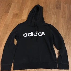 Svart hoodie från Adidas - Säljer en svart hoodie från Adidas med stor vit logga på bröstet. Tröjan har huva med dragsko och långa ärmar. 