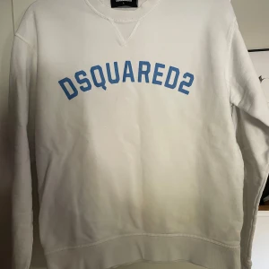 Vit sweatshirt från Dsquared2 - Säljer (åt min bror) en vit sweatshirt från Dsquared2 med blå text på bröstet. Tröjan har rund halsringning och långa ärmar. Klassisk och stilren design med normal passform, perfekt för en avslappnad look. Nypris 3200kr