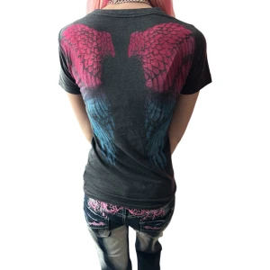 Svart t-shirt med vingar från Sinful - Cool svart t-shirt från Sinful med tryck av stora vingar i rosa och blått på ryggen och logga framtill. T-shirten har rund hals och korta ärmar, perfekt för en edgy streetstil.