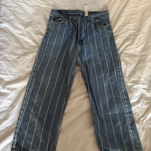 Blå randiga jeans från UNI JEAN - Säljer ett par blå jeans från UNI JEAN med vita ränder. Jeansen har raka ben och är lite kortare i längden. 