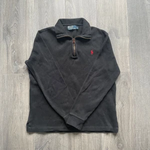 Ralph Lauren quarter zip - Säljer en klassisk svart quarter zip tröja från Polo Ralph Lauren. Tröjan har en röd broderad logga på bröstet och är tillverkad i bomull. Något urtvättad färg men inget som riktigt påverkar utseendet😁