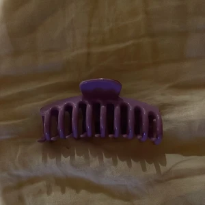 Set med tre hårklämmor i olika färger - Säljer ett set med tre hårklämmor i plast, perfekta för att snabbt och enkelt sätta upp håret. En klämma är lila, en är ljusblå och en är svart. Alla har klassisk form med breda taggar för bra grepp.