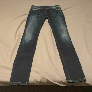 Replay mörkblå jeansbyxor - Säljer ett par mörkblå Replay jeans med klassisk femficksdesign och diskreta slitningar framtill, med snygga detaljer på bakfickorna och guldfärgade sömmar. Perfekta för en stilren vardagslook. Bara testade en gång. Storleken är W26 men passar även W27. Otroligt bra skick och köpta från början för 799.
