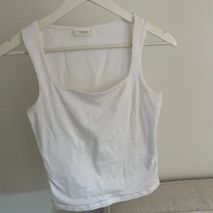 Vit linnetopp - Säljer en klassisk vit linnetopp med breda axelband och rundad halsringning. Perfekt basplagg i garderoben, enkel att matcha till olika outfits. Mjukt och bekvämt material.