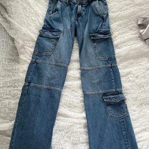 Blå cargojeans från Zara - Säljer ett par blå cargopants från Zara med flera stora fickor på sidorna och raka ben. Byxorna är tillverkade i klassiskt jeansmaterial. Perfekta för en avslappnad och trendig stil.