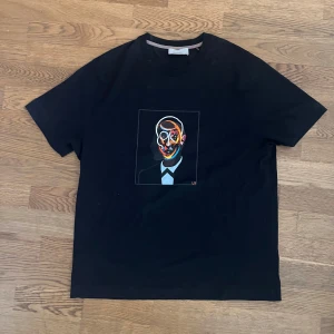 Svart t-shirt med färgstarkt konstmotiv från Limitato - Säljer en svart t-shirt med box från Limitato som är använd en gång, med ett unikt, färgstarkt konstmotiv av ett ansikte på bröstet. T-shirten har klassisk passform och är tillverkad i mjuk bomull. Perfekt för dig som gillar statement-plagg och konstnärlig stil. Priset går att diskutera vid snabb affär!!
