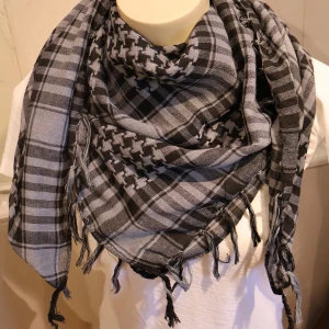 Palestina sjal Svart och grå rutig halsduk med fransar - Säljer en klassisk svart och grå rutig halsduk med fransar i kanterna. Halsduken har ett traditionellt mönster och är mjuk och lätt att bära. Perfekt för att ge din outfit en cool touch.