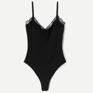 Svart Body - Snygg svart bodysuit med tunna axelband och v-ringning dekorerad med spets. Perfekt att styla till både jeans och kjol för en trendig look. Den är helt oanvänd och lappen sitter kvar! 