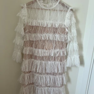 Vit spetsklänning med volanger från By Malina - Superfin vit spetsklänning från By Malina med flera lager volanger och lång ärm. Helt ny med lappar kvar. Stl M.  Nypris ca 2800kr