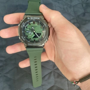 Grön G-Shock klocka - Säljer en robust G-Shock klocka med grön urtavla och matchande grön silikonrem. Klockan har digitala och analoga visare, svart boett och tydliga vita detaljer. Perfekt accessoar för dig som gillar sportig stil.