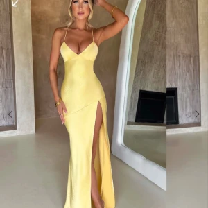 Gul långklänning med slits och öppen rygg - Säljer en elegant gul långklänning med smala axelband, djup v-ringning och hög slits framtill. Klänningen har öppen rygg med snörning och är figurnära upptill. Perfekt för balen!