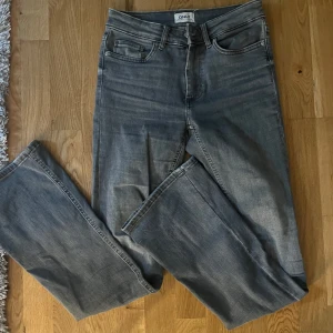 Grå jeansbyxor från ONLY - Säljer ett par grå jeansbyxor från ONLY med klassisk femficksdesign och hög midja. Jeansen har raka ben och subtila slitningar för en avslappnad look. Perfekta till vardags och enkla att matcha med olika toppar.