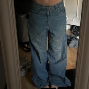 Blåa vida jeans med låg midja - Säljer ett par blåa jeans med riktigt vid passform och låg midja. Jeansen har klassisk femficksdesign och stängs med dragkedja och knapp. Perfekta för dig som gillar en avslappnad och trendig look. Jag har gått mycket med dom och på dom då dom varit långa, så nertill är de ganska slitna.