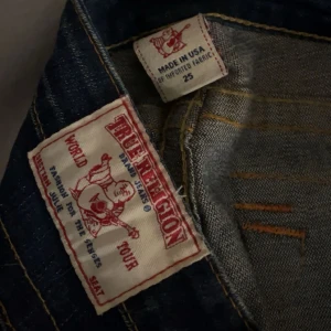 True Religion lågmidjade jeans med skinny  - Mörkblå jeans från True Religion med skinny och råa, fransiga benslut. Säljer för jag använder inte skinny jeans dom är vintage de är därför dom kan se lite ”slitna” ut men annars helt vanligt. Som ni ser på bild 4 så skulle jag sy dom till utsvänga men gjorde aldrig det. Går nog lätt att sy till eller bara bära dom som dom är 