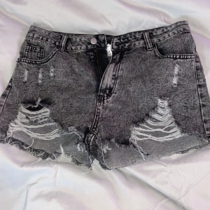 Grå jeansshorts med slitningar - Snygga grå jeansshorts med kraftiga slitningar och fransig kant. Klassisk femficksmodell med knapp och dragkedja framtill. Perfekta för en avslappnad stil.