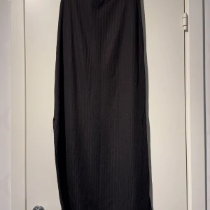 Svart ribbad kjol med slits - Säljer en svart kjol i ribbat material med en snygg slits på sidan. Kjolen har en enkel och stilren design som passar perfekt till olika tillfällen. Materialet är stretchigt och följsamt.