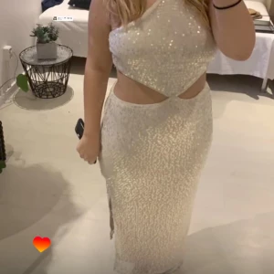 Glittrig champagnefärgad långklänning med slits - Säljer en glittrig långklänning i champagnefärg med smala axelband och snygg cut-out vid midjan. Klänningen har en slits på sidan och är täckt av paljetter som ger ett lyxigt intryck. Perfekt för bal eller fest! 💫