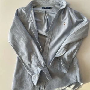 Ljusblå skjorta från Ralph Lauren - Säljer en klassisk ljusblå skjorta från Ralph Lauren i slim fit-modell. Skjortan är aldrig använd, så den är i mycket bra skick. Pris kan diskuteras vid snabb affär!